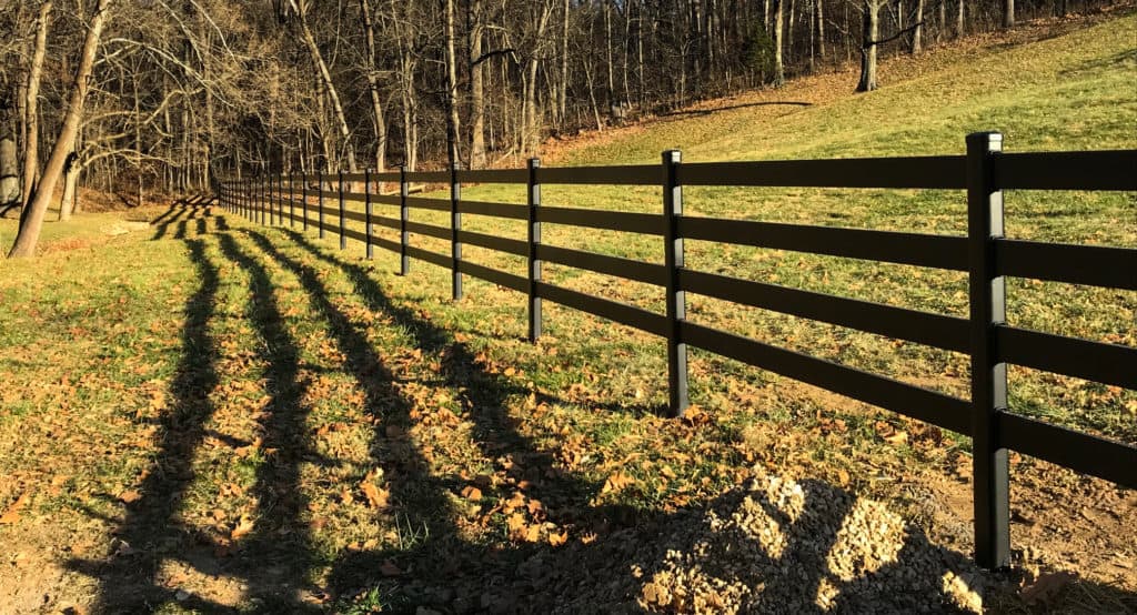 Black four-rail Buckley steel board horse fence running along a pasture slope