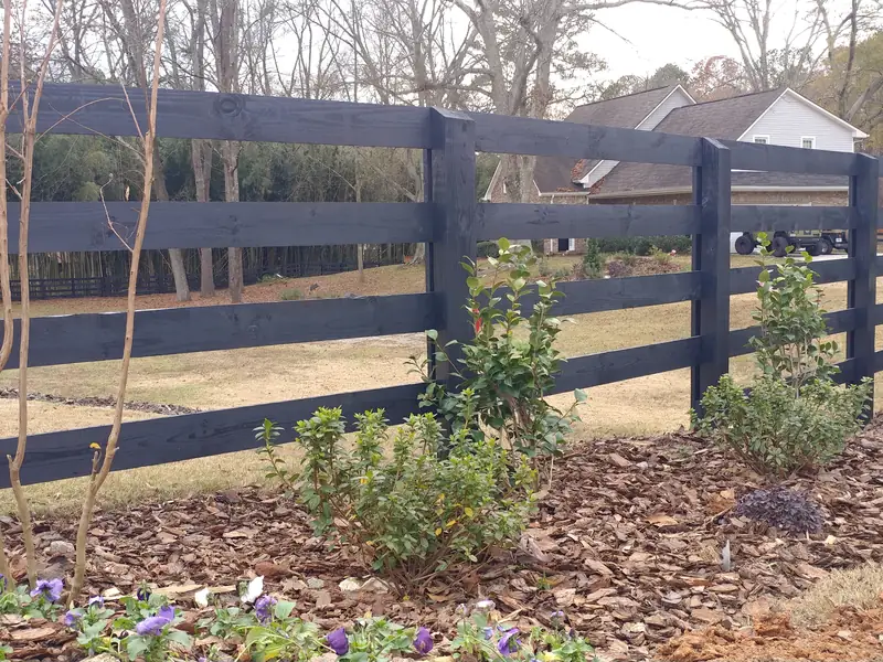 Black four-rail ranch rail fence with landscaping