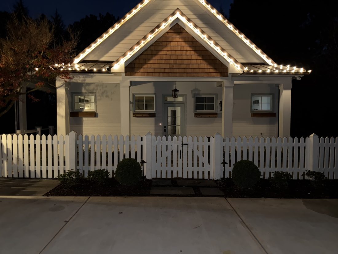 White wood picket fence and gate fronting a lantern-lit Alpharetta, GA cottage, built by FenceWorks of Georgia